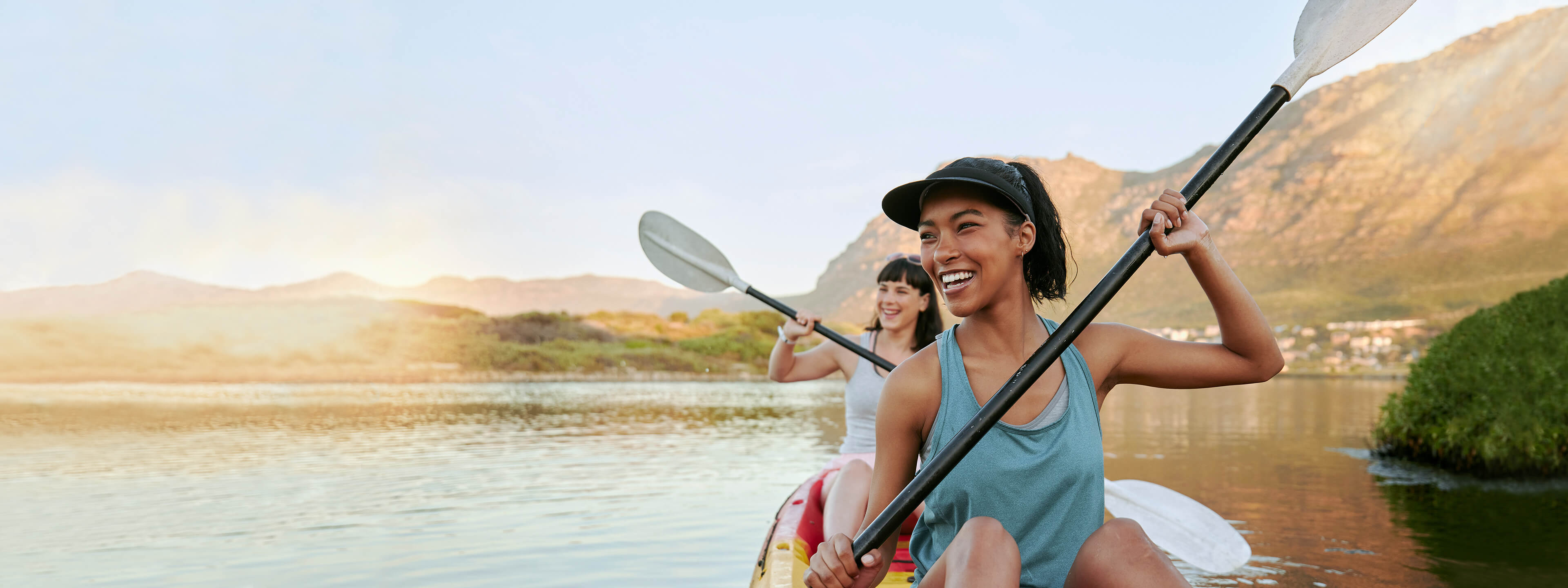 Two women paddling kayak on lake with mountain views